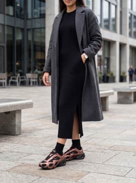 Air Max Muse Rose Gold – A sleek, black rib-knit midi dress with a side slit, layered under an oversized charcoal grey wool overcoat to create a sophisticated contrast between formal tailoring and futuristic footwear.