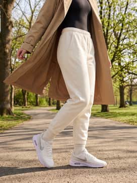 Air Max Nuaxis Se – Cream-colored joggers with a tucked-in black bodysuit and a long tan trench coat for a sophisticated, elevated streetwear vibe.