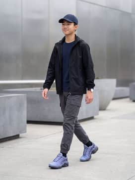 Charcoal grey cargo joggers paired with a black tech-fabric windbreaker and a navy baseball cap for a modern utility look.