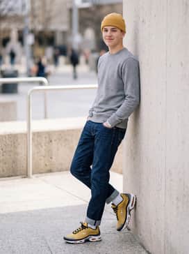 Slim-fit raw indigo denim jeans cuffed at the ankle, worn with a simple grey heather crewneck sweatshirt and a yellow beanie that echoes the shoe's primary color.