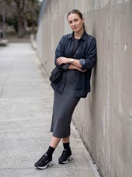 A charcoal grey ribbed knit midi dress layered with an oversized denim shirt and a crossbody utility bag for a comfortable city look.