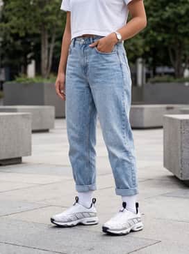 Light-wash baggy mom jeans with a small white crop top, layered with an unbuttoned oversized flannel shirt and silver hoop earrings.