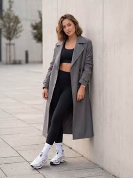 Black high-performance leggings and a matching sports bra under a long grey trench coat for a sophisticated urban athleisure outfit.