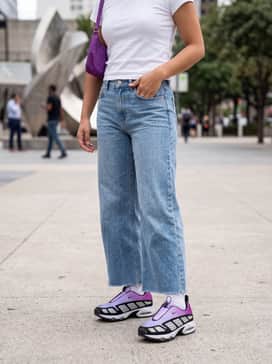 Wide-leg light-wash denim jeans with a raw hem, a fitted white baby tee, and a small purple nylon shoulder bag to match the shoe's gradient.
