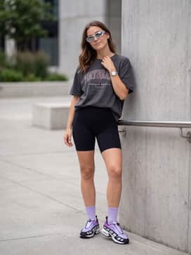 Air Max Sndr – High-waisted black biker shorts, an oversized charcoal grey graphic t-shirt, and silver-rimmed futuristic sunglasses for an off-duty look.