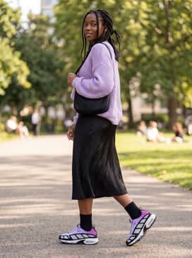 A black satin midi skirt paired with a chunky lavender knit sweater and silver jewelry to create a high-fashion contrast between soft textures and technical footwear.