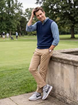 A clean, smart-casual outfit pairing tan chino pants with a tucked-in light blue chambray shirt and a navy wool sweater vest.
