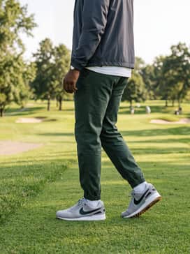 A sporty weekend vibe consisting of dark green joggers, a crisp white graphic tee, and a neutral-toned windbreaker.