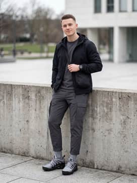 Tapered charcoal cargo trousers, a black technical windbreaker, and a minimalist crossbody bag for a sleek 'gorpcore' appearance.