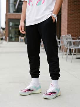 A casual urban outfit consisting of tapered black joggers, an oversized white graphic tee with pink lettering, and a sleek black nylon windbreaker.