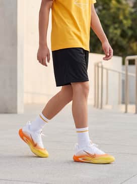 Black moisture-wicking mesh athletic shorts paired with a bright yellow graphic t-shirt and white crew socks to highlight the shoe's vibrant gradient.