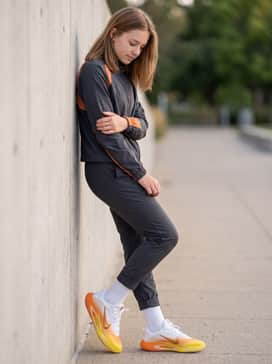 Aone Se – Slim-fit dark wash denim with a clean cuff at the ankle to showcase the metallic accents, worn with a coordinated orange-themed windbreaker.