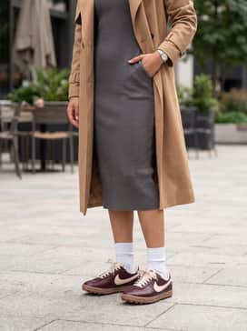 An oversized camel trench coat worn over a neutral-toned midi rib-knit dress, finishing the look with these sneakers for a balanced blend of sophistication and comfort.