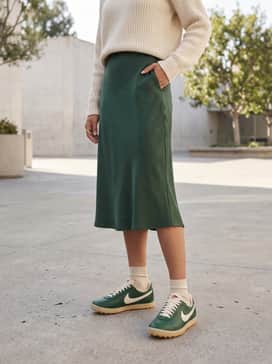 A forest green satin midi skirt worn with a chunky cream knit sweater and gold hoop earrings to lean into a sophisticated, monochromatic earthy palette.