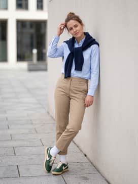 Cropped khaki chinos and a crisp light blue button-down shirt, finished with a navy blue wool sweater draped over the shoulders for a timeless collegiate aesthetic.