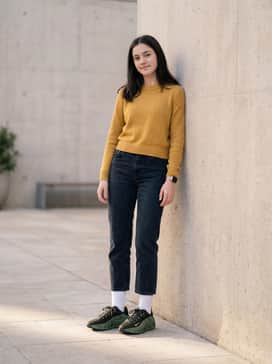 Dark-wash cropped denim jeans worn with white crew socks and a mustard yellow knit sweater that highlights the subtle yellow accents on the shoe's branding.