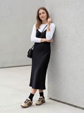 A black midi-length slip dress layered over a fitted white long-sleeve tee, finished with a small black leather crossbody bag for a 90s-inspired feminine vibe.