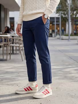 Tapered navy chinos and a cream-colored cable knit sweater, accessorized with a leather strap watch to lean into a sophisticated preppy style.