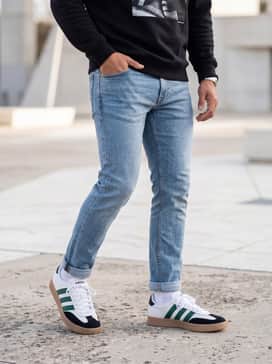 Barreda Shoes – Light-wash slim-fit jeans rolled at the cuff, worn with a black graphic sweatshirt and a minimalist baseball cap for a clean streetwear look.
