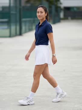 Barricade 13 Tennis Shoes – A white pleated tennis skirt paired with a navy blue moisture-wicking polo shirt and white quarter-length athletic socks for a classic, professional court-ready look.