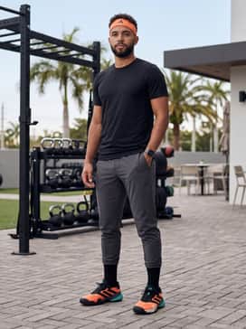 A modern gym ensemble consisting of tapered charcoal joggers, a compression-fit black t-shirt, and a matching orange performance headband.