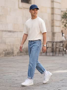 Light-wash straight-leg jeans with a tucked-in oversized cream graphic tee and a navy blue baseball cap for a classic 90s street look.