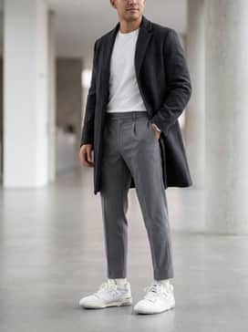 Bb550 – Neutral-toned pleated trousers paired with a crisp white button-down shirt and a grey wool overcoat for a sophisticated smart-casual ensemble.