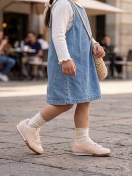 Bella Donna Pearls Little Kids Easy On Sneakers – A light-wash denim jumper dress layered over a white pointelle-knit long-sleeve shirt with matching ruffled socks.