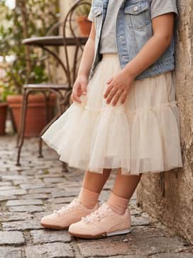 Bella Donna Pearls Little Kids Easy On Sneakers – A cream-colored tulle tutu skirt worn with a simple grey heathered tee and a denim vest for a high-low fashion statement.