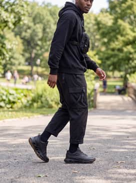 Biom 720 Goretex – Black utility trousers featuring straps and extra pockets, matched with an oversized black graphic hoodie and a chest rig bag to lean into a modern techwear aesthetic.