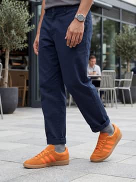 Dark navy chinos and a crisp white Oxford shirt worn open over a charcoal grey tank top, creating a smart-casual ensemble that lets the orange pop.
