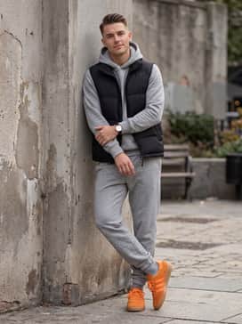 Brmd Shoes – Grey melange joggers with a matching hoodie and a black puffer vest for a sporty, monochromatic athleisure outfit that anchors on the vibrant footwear.
