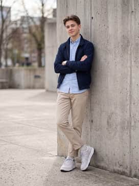 Tapered sand-colored chinos worn with a light blue oxford button-down shirt tucked in and a navy blue Harrington jacket.