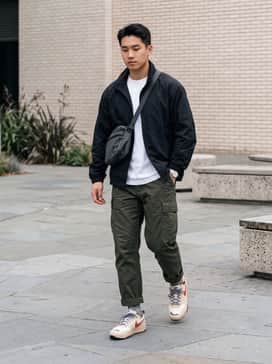 Olive green tapered cargo pants paired with a black technical windbreaker and a crisp white moisture-wicking tee for a functional, utility-driven look.
