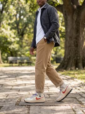Tan corduroy trousers combined with a white oxford button-down shirt layered under a charcoal grey wool overshirt for a textured, transitional weather vibe.