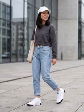 High-waisted light wash mom jeans paired with a cropped charcoal sweatshirt and a matching white baseball cap for a classic weekend look.