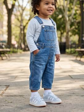 Dark-wash denim overalls worn over a crisp white long-sleeve tee to create a classic, timeless playground aesthetic.