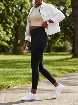 Sporty Edge: Black high-performance leggings, a cropped ribbed tank top in sand, and an unbuttoned white denim jacket for a modern athletic vibe.