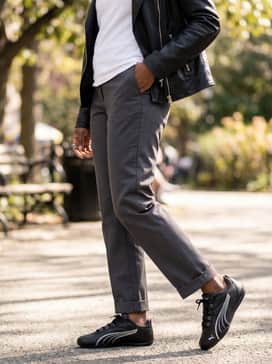 Straight-leg charcoal trousers with a tucked-in white t-shirt and a black leather moto jacket for a sharp streetwear aesthetic.