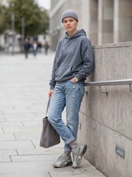 A modern streetwear outfit consisting of light-wash distressed denim, a vintage-style graphic hoodie in slate grey, and a crossbody messenger bag.