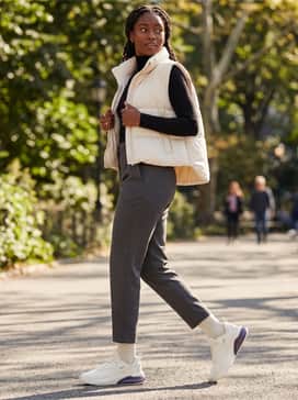 Cell Thrill Womens Running Shoes – Tapered charcoal grey joggers worn with a slim-fit black turtleneck and a structured cream puffer vest for a polished yet functional commuter outfit.