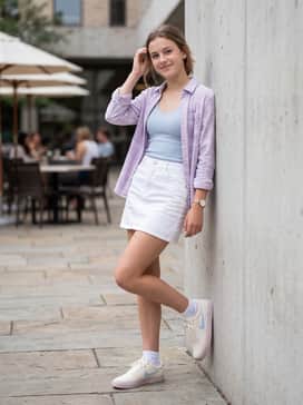 A white denim mini skirt styled with a light blue ribbed tank top and a thin lavender flannel shirt worn open.