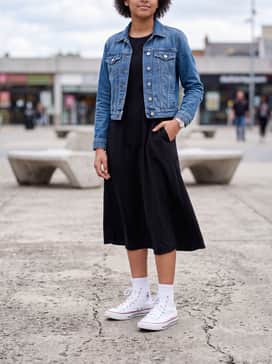 A black floral-print midi dress layered with a cropped blue denim jacket and accessorized with delicate silver jewellery for a feminine yet edgy vibe.