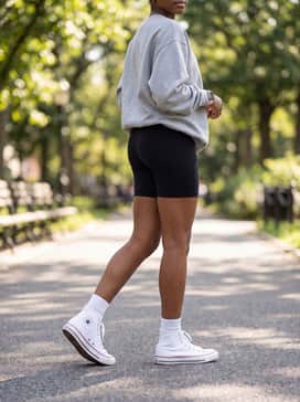High-waisted black biker shorts paired with a grey oversized collegiate sweatshirt and tall white crew socks for a trendy athleisure look.