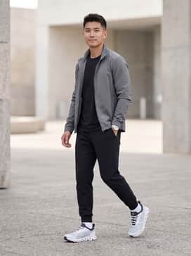 A monochromatic look featuring black tapered joggers, a matching technical t-shirt, and a grey windbreaker for a sleek street-to-gym transition.