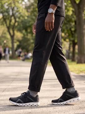 A sophisticated athleisure set pairing tailored black tech chinos with a sage green quarter-zip pullover and a sleek sports watch, perfect for transitioning from a light workout to a coffee date.