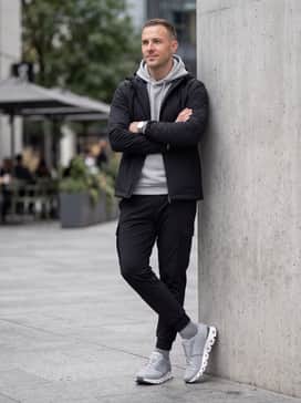 Black tapered technical joggers with cargo pockets, a light grey tech-fleece hoodie, and a matte black waterproof shell jacket for a modern techwear look.