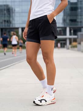 A sleek track-ready look consisting of high-performance black compression leggings, a fitted orange tech-fabric tank, and a lightweight white running visor.