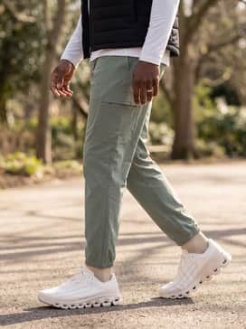 Combine the shoes with sage green technical cargo pants, a white long-sleeve base layer, and a black quilted gilet for a functional yet stylish outdoor athletic outfit.