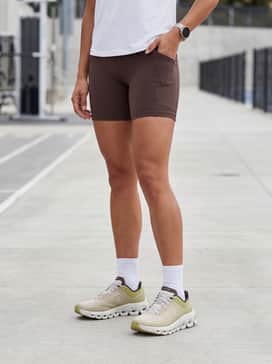 Cloudflow 4 – Biker shorts in a deep mocha brown paired with a cropped, moisture-wicking white technical tee and thin white crew socks to highlight the shoe's midsole.
